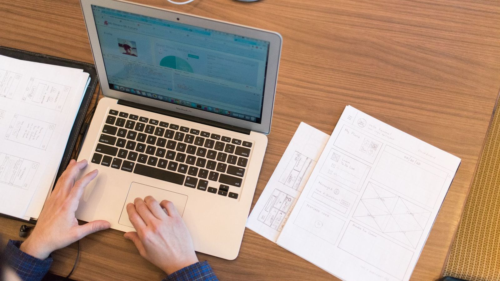 Des mains qui saisissent des notes sur un ordinateur portable, entourées de documents